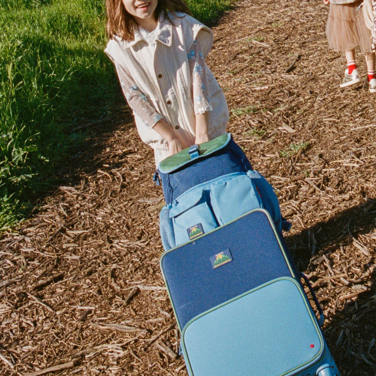 Girl pulling STATE Bags Logan Carry-On Suitcase Green/Blue/Orange 