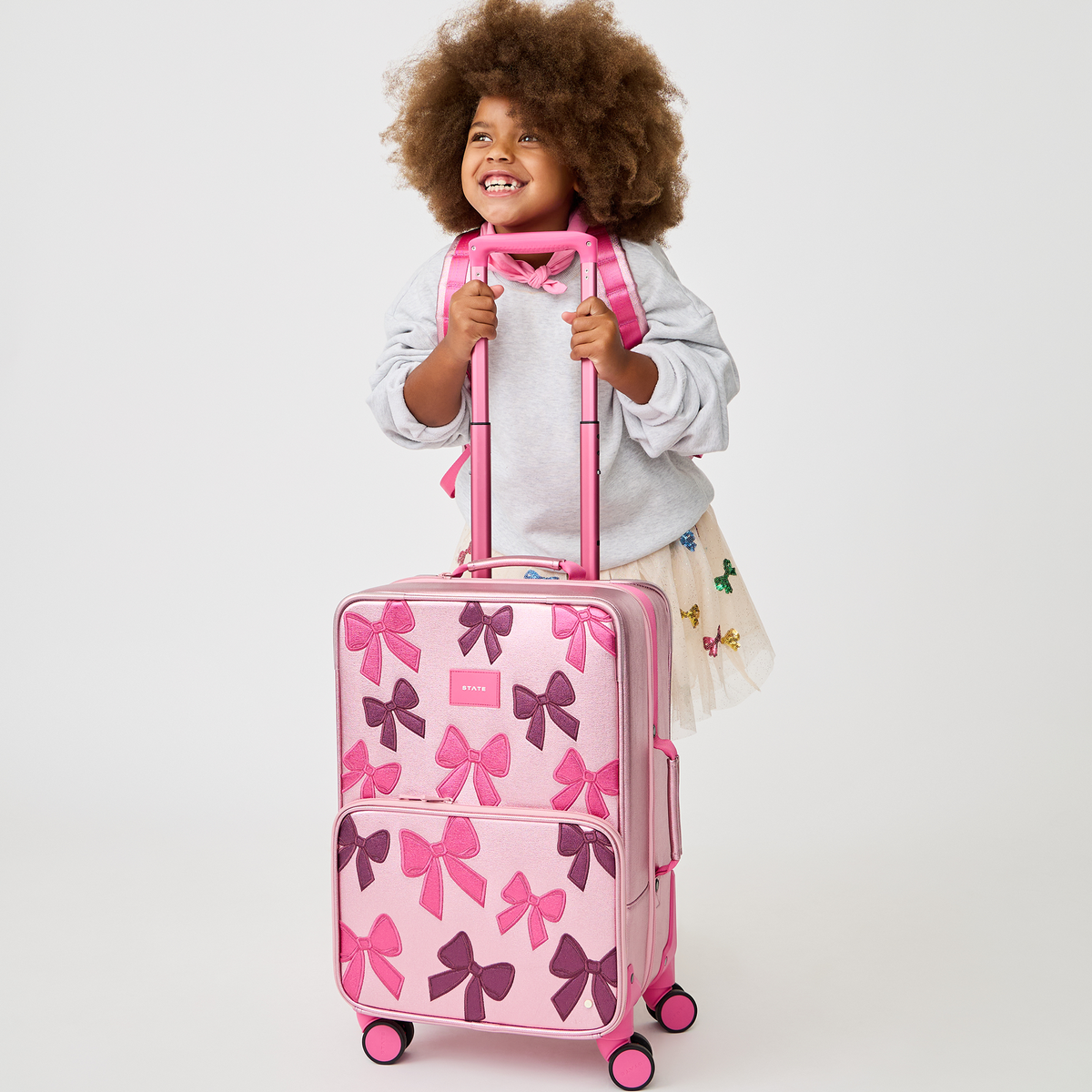 girl pushing STATE Bags Logan Carry-On Suitcase Bows