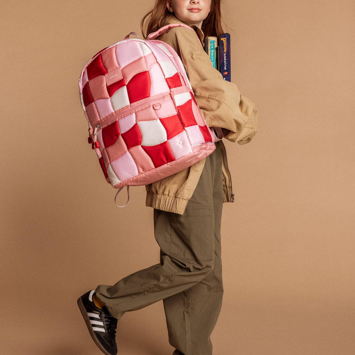 Girl wearing state bags kane pink puffer check backpack while carrying books