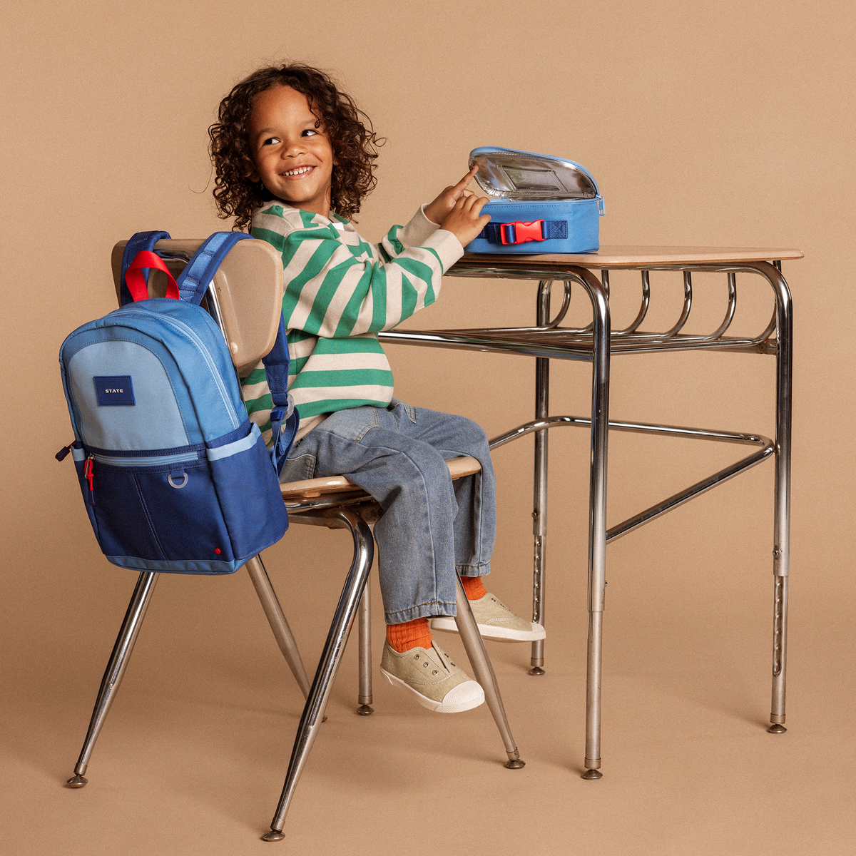 Boy sitting at desk with state bags kane mini bakpack blue colorblock