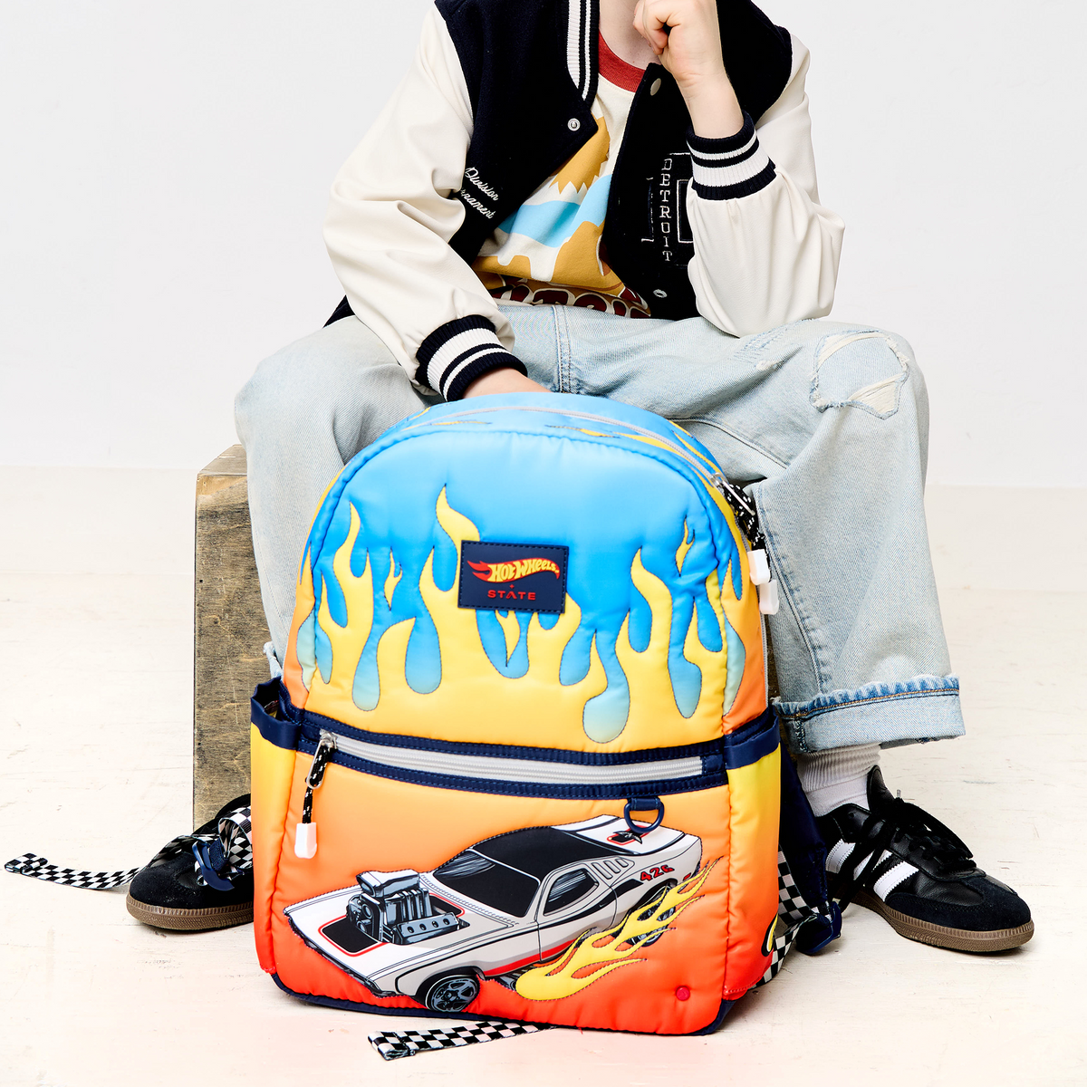 Boy sitting with STATE Bags x Hot Wheels Kane Backpack Hot Wheels Flames 