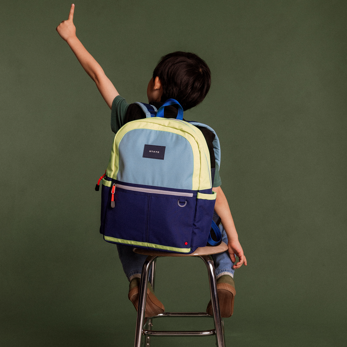 Boy sitting in chair wearing kane backpack navy/neon