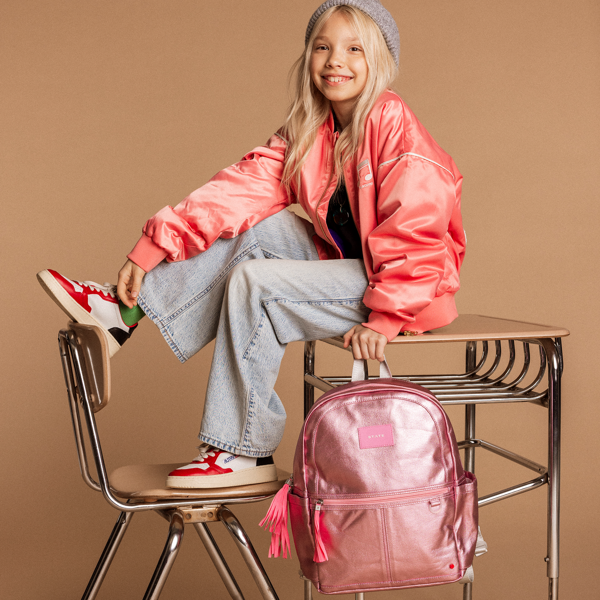 Girl sitting on desk holding Kane Kids Pink/Silver Backpack
