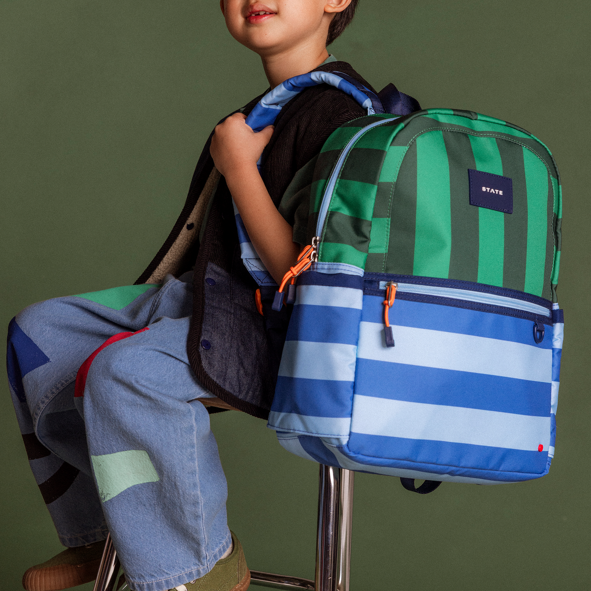 boy wearing state bags kane backpack stripes in a chair