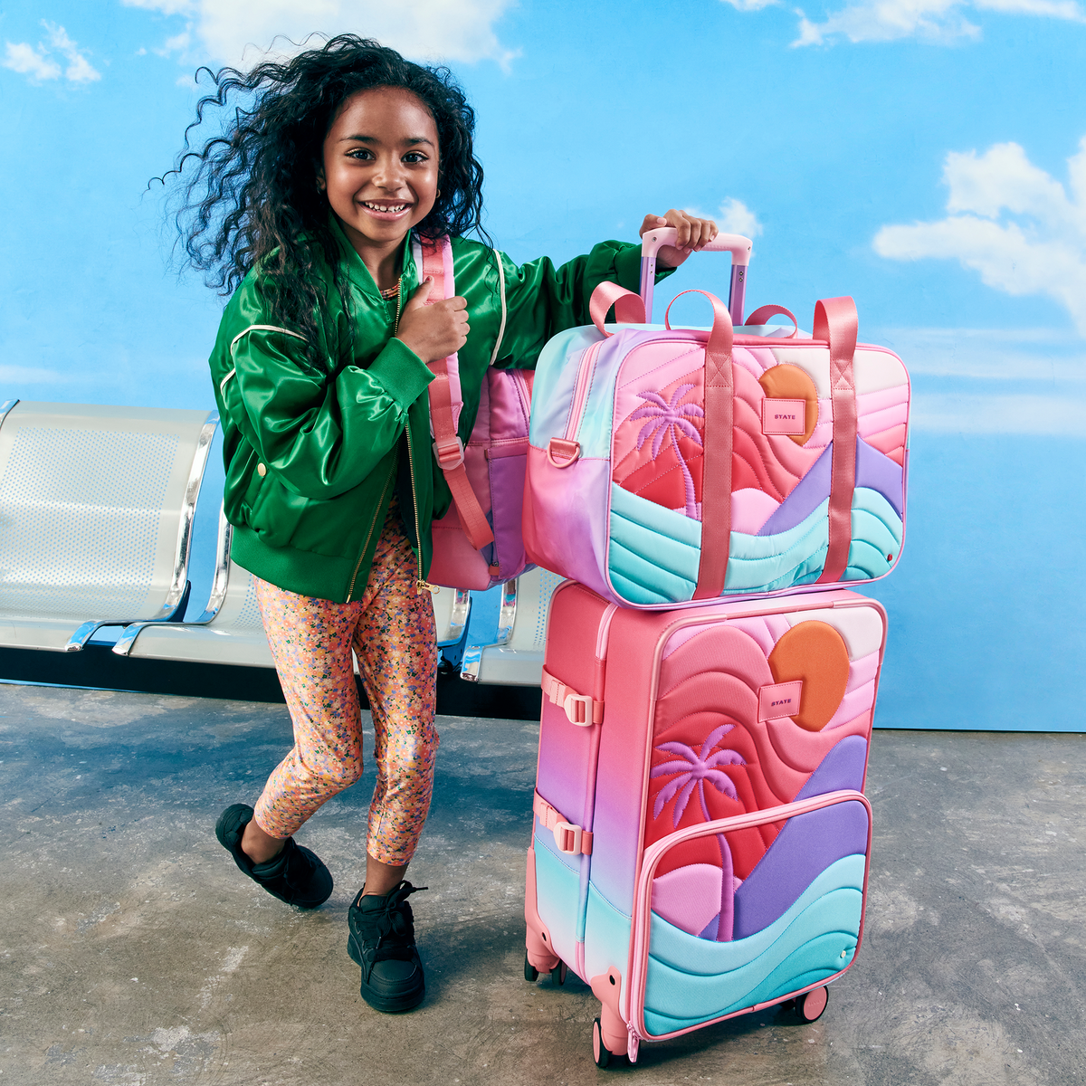 Girl running holding state bags sunset puffer logan carry-on suitcase and rockaway duffle