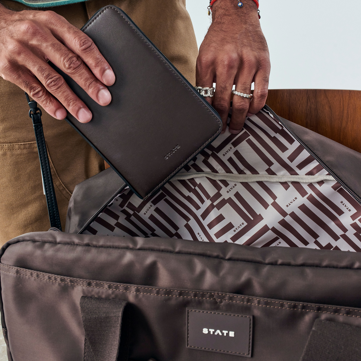 Man putting STATE Bags Passport Holder Brown into wellington weekender brown