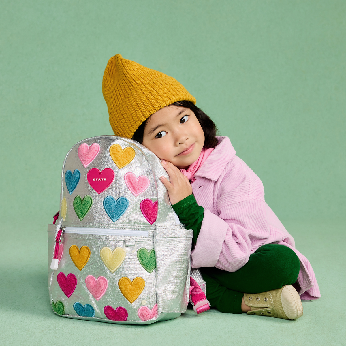 girl sitting with STATE Bags Kane Mini Backpack Happy Fuzzy Hearts