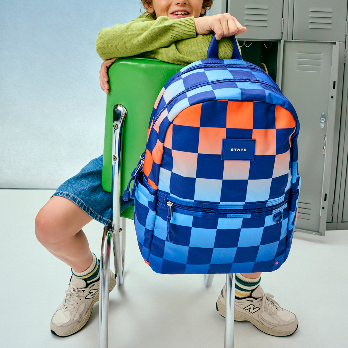 boy sitting holding kane double pocket backpack blue checkerboard 