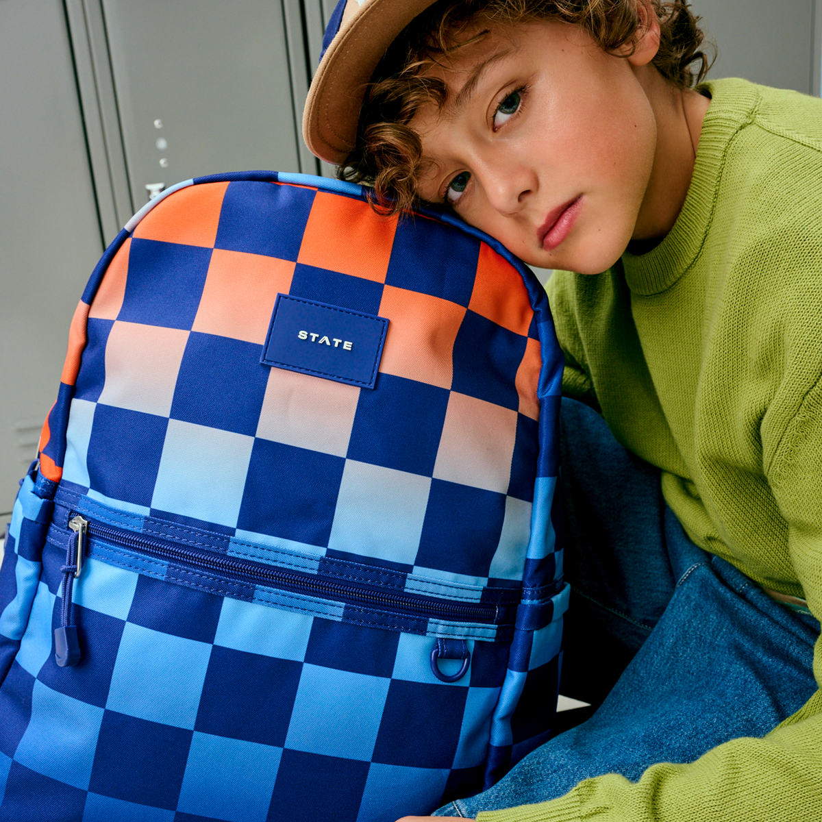 boy sitting holding kane double pocket backpack blue checkerboard 